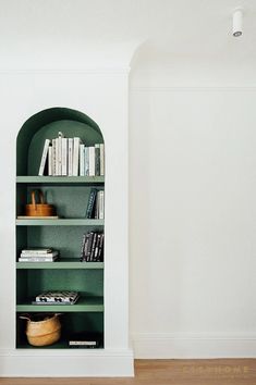 a green book shelf with books on it in the corner next to a white wall