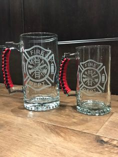 two fire department glass mugs with red string bracelets sitting on a wooden table