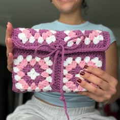 a woman holding up a crocheted purse with pink and white flowers on it