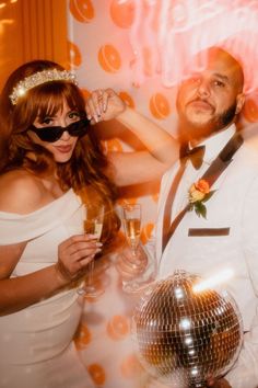 a man and woman posing for a photo in front of a disco ball holding champagne glasses