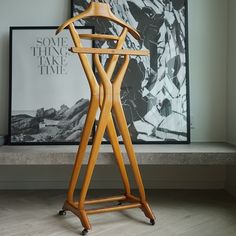 a wooden coat rack sitting on top of a hard wood floor next to a painting