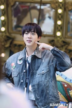 a young man wearing a denim jacket and tie standing in front of a mirror with his finger to his mouth