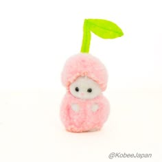 a small pink stuffed animal with a green leaf on it's head, sitting in front of a white background