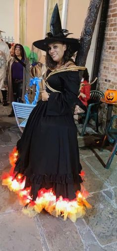 a woman dressed as a witch in a black dress and hat with flames on the ground