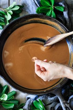 a person holding a spoon in a pan filled with chocolate sauce and leaves on the side