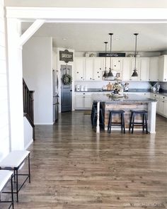 an open kitchen and dining room with white cabinets, wood flooring and stainless steel appliances