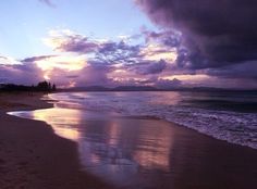 the sun is setting at the beach with clouds in the sky and people walking on the sand