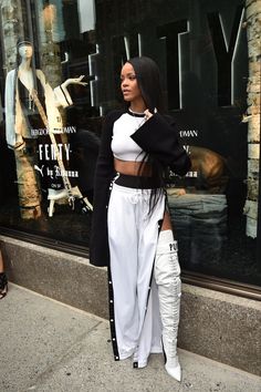 a woman standing in front of a store window wearing white pants and black jacket with high heels