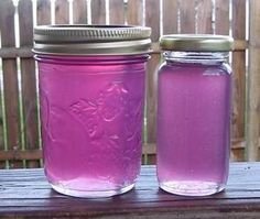 two jars filled with purple liquid sitting on top of a wooden table next to a fence