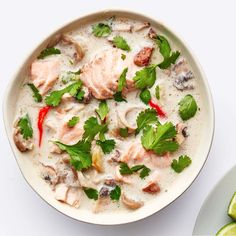 a white bowl filled with meat and cilantro next to a plate of limes