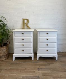 two white dressers with gold letters on them and a potted plant in the corner