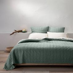 a bed with green bedspread and pillows in a white room next to a wall