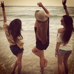 three women standing on the beach with their arms in the air and looking at the ocean