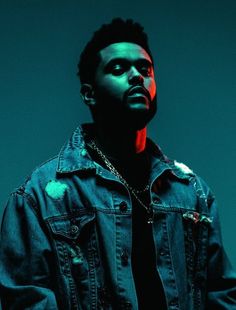 a man wearing a denim jacket and chain around his neck, standing in front of a blue background