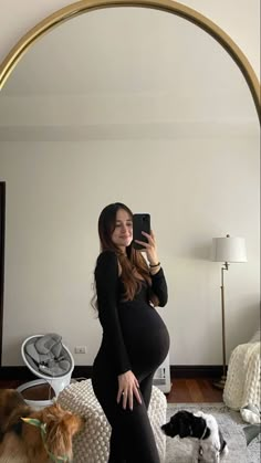 a pregnant woman taking a selfie in front of a mirror with her dogs on the floor