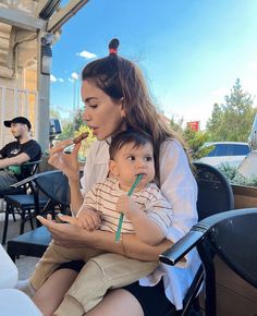 a woman holding a baby while sitting on top of a chair with a straw in her mouth