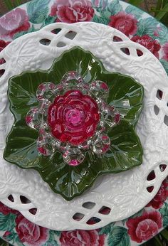 a plate with a flower on it sitting in the middle of some green and red flowers