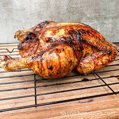 a cooked chicken sitting on top of a wooden table next to a metal grate