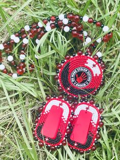 two red and white beaded earrings laying on top of grass next to each other