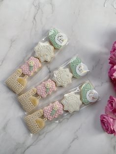 four decorated cookies sitting on top of a white counter next to pink carnations