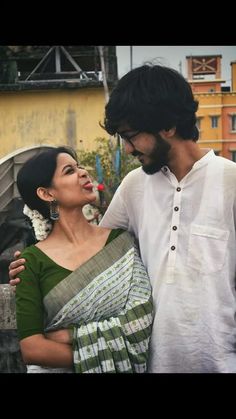 a man and woman standing next to each other in front of a building with buildings behind them