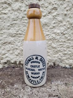 a bottle that is sitting on the ground next to a white wall and cement floor