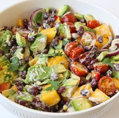 a salad in a white bowl with tomatoes, avocado, and other vegetables