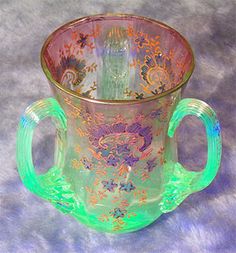 an ornate glass cup with green handles on a blue background