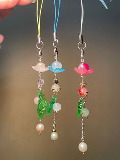 three different colored glass beads hanging from hooks on a string with pearls and chains attached to them