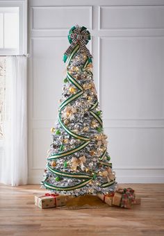 a christmas tree with presents under it on the floor in front of a white wall