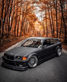 a black car parked on the side of a road in front of trees with orange leaves