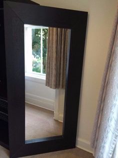 a large mirror sitting in the middle of a living room next to a window with curtains