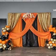 an orange, black and gold balloon arch is decorated with flowers on the top floor