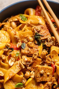 a bowl filled with noodles and vegetables next to chopsticks on a table top