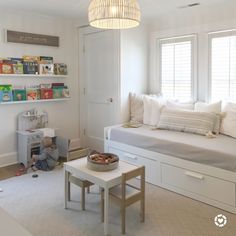 a room with a bed, bookshelf, and table in front of the window