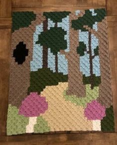 a crocheted rug with trees and flowers on the floor in front of a wooden floor