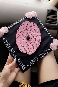 a person holding a decorated graduation cap with pink flowers on the front and side of their head