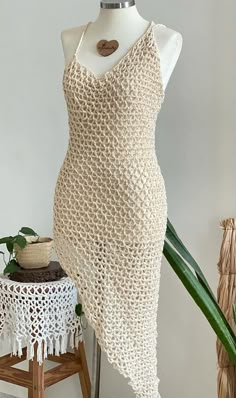 a white crocheted dress on a mannequin next to a potted plant