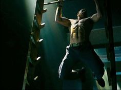 a shirtless man hanging from a ladder in the dark