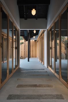 an empty hallway with wooden doors leading to another room in the background and lights hanging from the ceiling