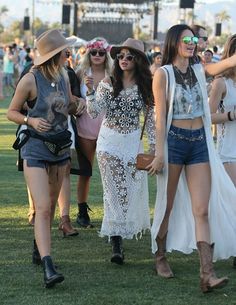 two women in short shorts and cowboy hats walk through the grass at an outdoor music festival