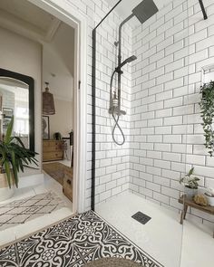 a white tiled bathroom with a walk in shower next to a potted green plant