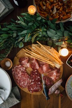 a wooden table topped with meats and cheeses on top of plates next to candles