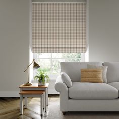 a living room with a couch, coffee table and window covered in plaid roman shades