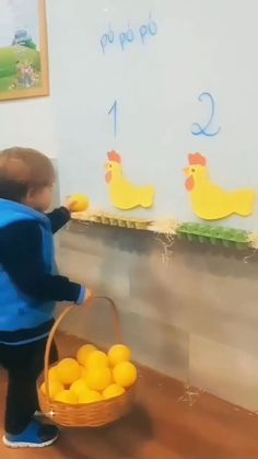 a little boy standing in front of a whiteboard holding a basket of oranges