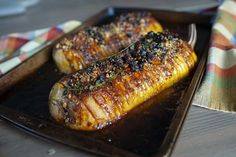 two grilled corn on the cob are sitting on a black tray next to a colorful napkin