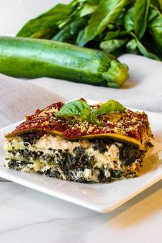 a slice of lasagna with spinach and cheese on a plate next to cucumbers