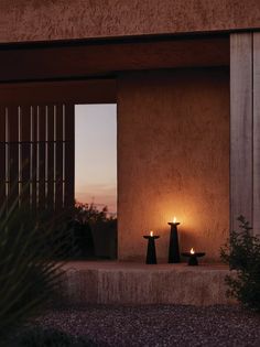 two candles sitting in front of a building with a window on one side and an open door to the other