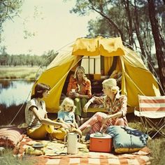 a group of people sitting on top of a blanket next to a yellow and white tent