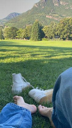 two people laying in the grass with their feet on each other's legs and mountains in the background